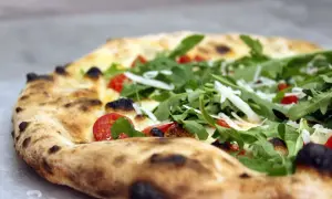 Zbliżenie na pizzę z rukolą, pomidorkami koktajlowymi i parmezanem.