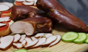 Aromatyczny, wędzony kurczak w całości i pokrojony w plastry, obok kanapek z pomidorem i plasterków ogórka.