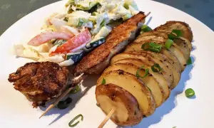 Idealne jakie mięso do pieczonych ziemniaków? Na talerzu szaszłyk z mięsa mielonego, grillowany kawałek mięsa i pieczone ziemniaki z cebulką, obok surówka.