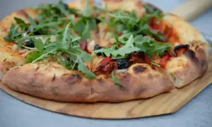 Pyszny spod od pizzy z rukolą, oliwkami i papryką, gotowy do podania.