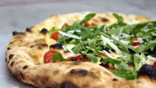 Zbliżenie na pizzę z rukolą, pomidorkami koktajlowymi i parmezanem.