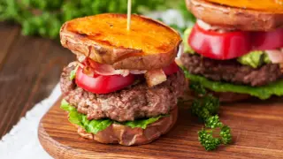 Pyszny burger na talerzu z soczystą wołowiną, chrupiącym bekonem, pomidorem i awokado, podany na słodkich ziemniakach.