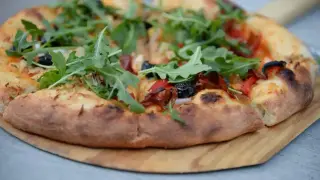 Pyszny spod od pizzy z rukolą, oliwkami i papryką, gotowy do podania.