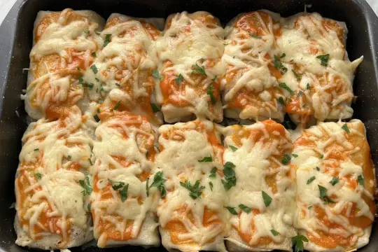 Zapiekane naleśniki z piersią z kurczaka, polane sosem pomidorowym i posypane ciągnącym się serem, ozdobione natką pietruszki.