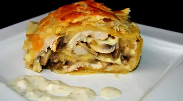 Pyszna pierś z kurczaka w cieście francuskim z pieczarkami i serem, podana z sosem.