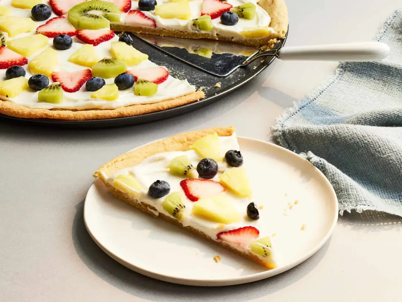 Słodkie ciasto na pizzę z kremem i owocami: truskawkami, kiwi, ananasem i borówkami. Idealne coś słodkiego z ciasta na pizzę.