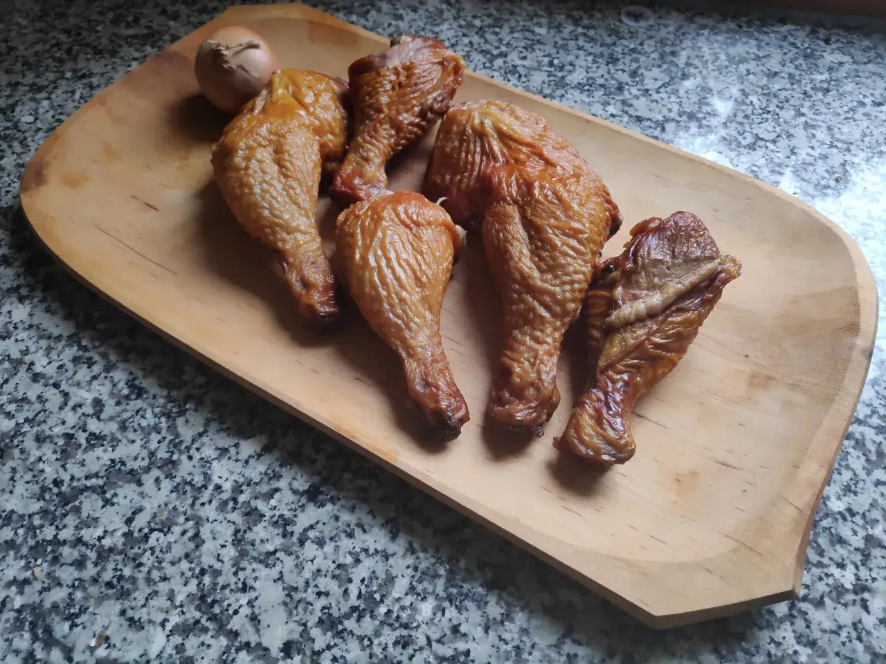 Pięć kawałków wędzonego kurczaka i cebula leżą na drewnianej desce.