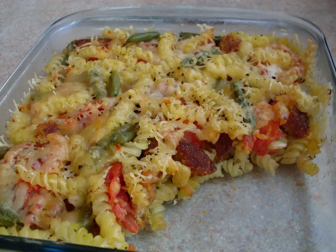 Zapiekanka z ugotowanego makaronu fusilli z kawałkami kiełbasy, fasolką szparagową i pomidorami, zapieczona pod serem.