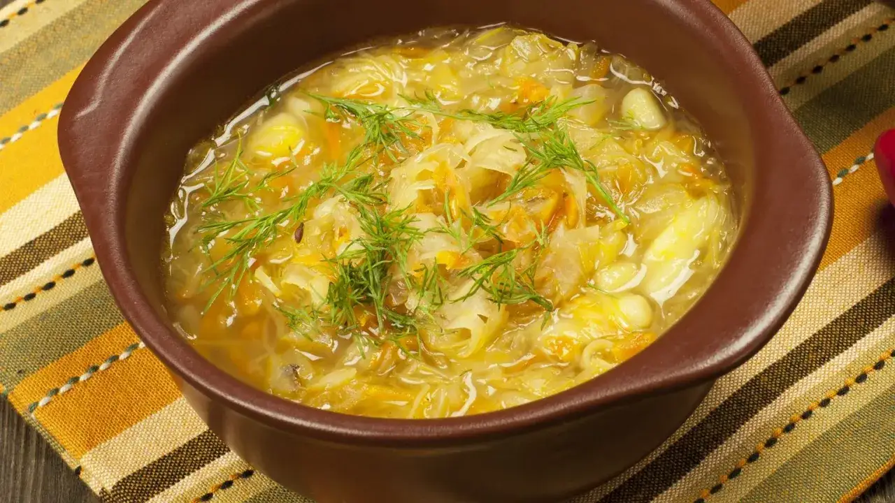 Gęsta zupa z białej kapusty z ziemniakami, ozdobiona świeżym koperkiem. Aromatyczne danie w brązowej miseczce.